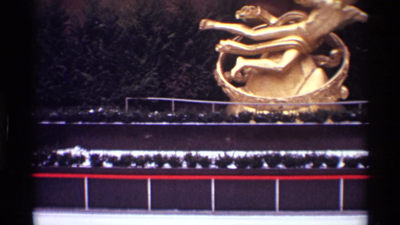 Golden outdoor sculpture above a dark facade with shrubs and a red trim line.