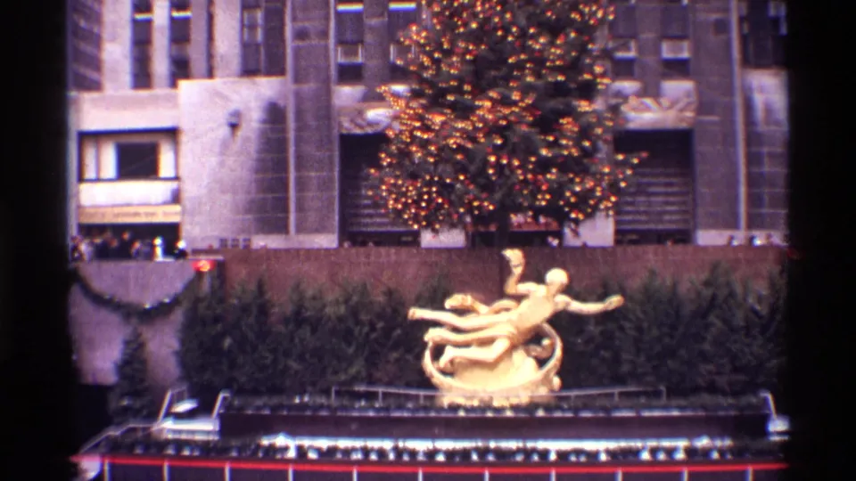 1970 New York City 8mm frame with an illuminated Christmas tree above a gilded sculpture and evergreen-lined display area.