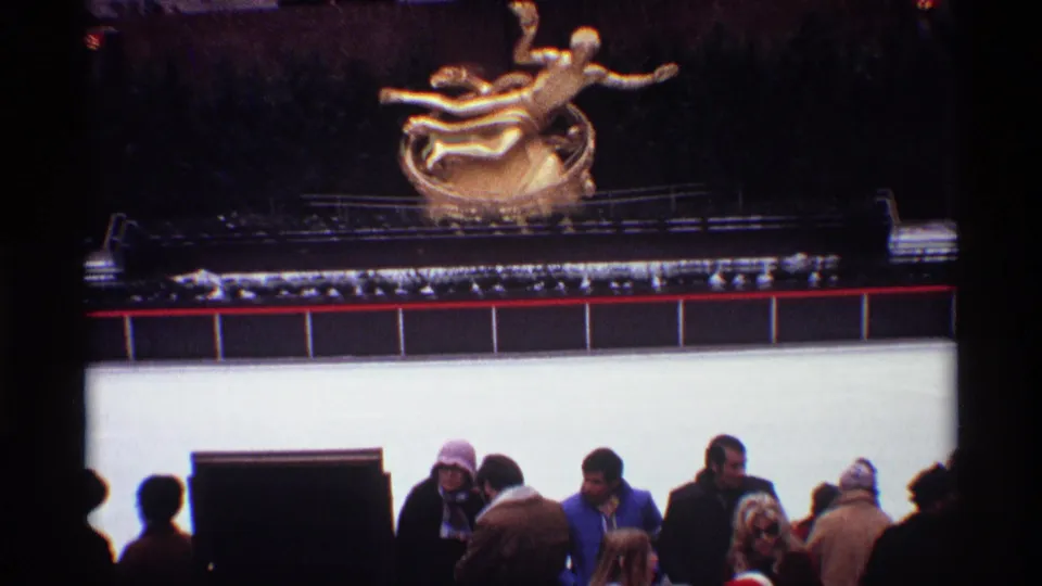 Underexposed 1970 Rockefeller Center view with the Prometheus sculpture above a rink barrier and a small winter crowd in the foreground.