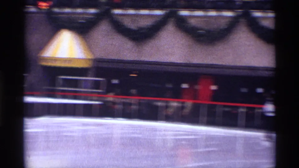 1970 New York City home-movie view of a mostly empty ice rink section with a striped awning, garlands, and a red railing.