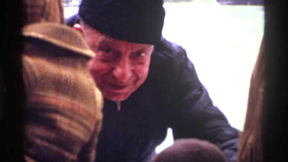 Close-up from the 1970 New York City rink outing showing a smiling man in a dark winter hat near other bundled visitors.