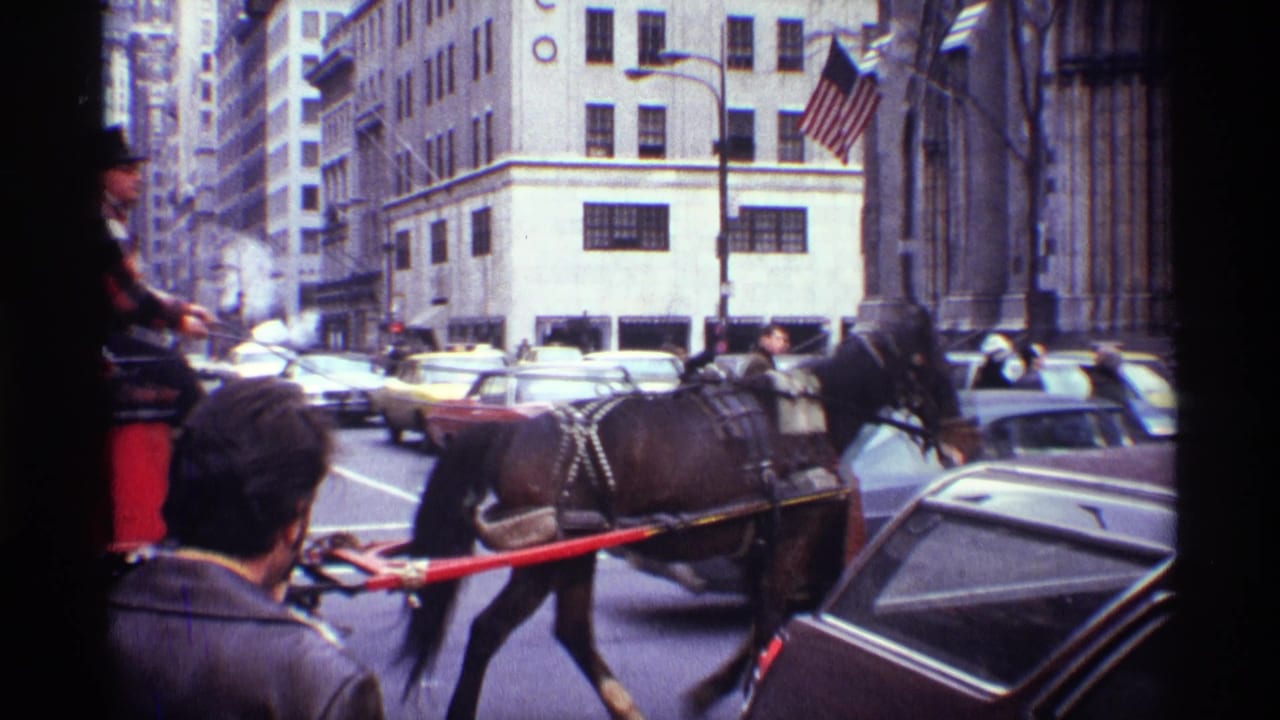 1970 New York City 8mm frame showing a dark horse pulling a carriage past cars, pedestrians, and tall stone buildings.