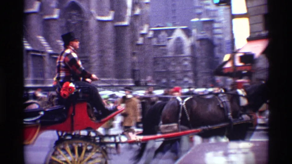 1970 New York City frame showing the carriage continuing along the street, with pedestrians, cars, stone architecture, and storefront awnings nearby.
