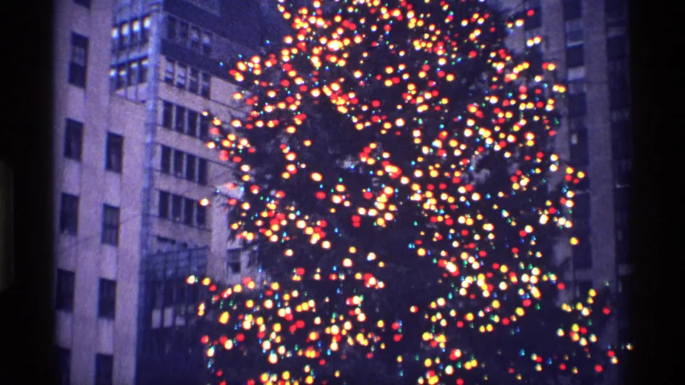 The 8mm frame shows a bright Christmas tree display surrounded by high-rise facades in New York City.
