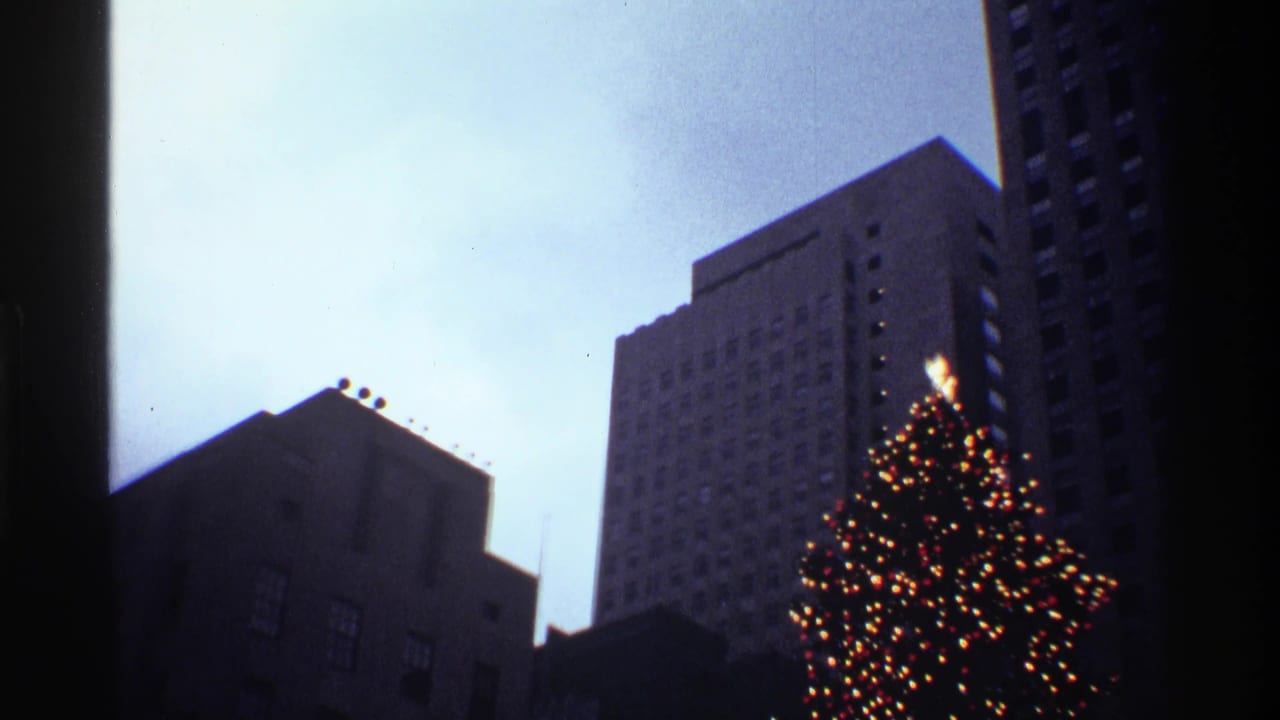 1970 New York City 8mm frame showing a decorated Christmas tree below tall buildings in cool evening light.