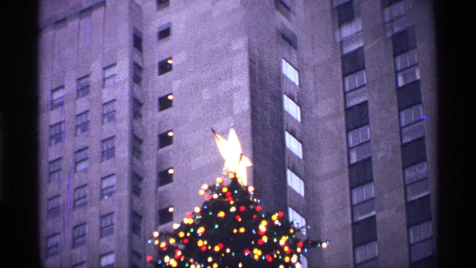 A closer 8mm view centers the bright tree-top star and colored lights against tall building facades.