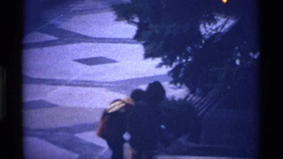 Soft 8mm close view of two bundled children partly obscured by darkness and tree shadow on a patterned city plaza.
