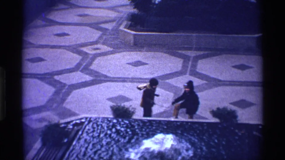 1970 New York City frame of two bundled children facing each other near a low edge, with patterned paving behind them.
