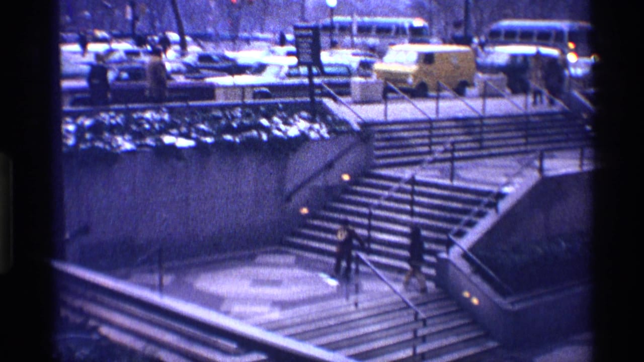 Two small figures run up broad concrete stairs near a busy street with buses and cars.