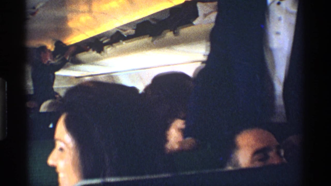 Passengers seated inside a dim railroad car with overhead racks and a woman in the foreground.