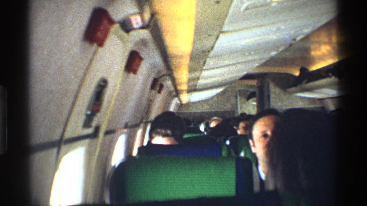 Passengers seated inside an airplane cabin with green seat backs and overhead compartments.