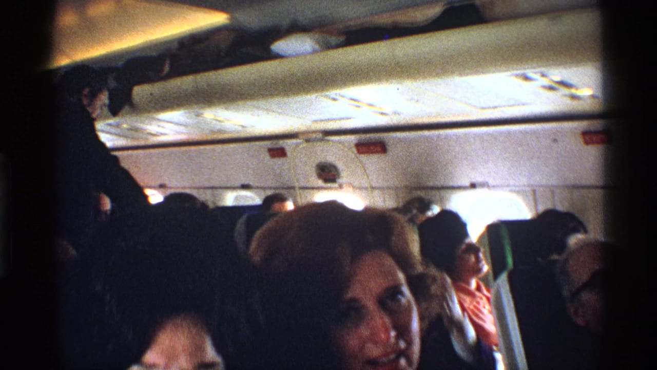 Passengers seated inside an airplane cabin as a woman faces the camera.
