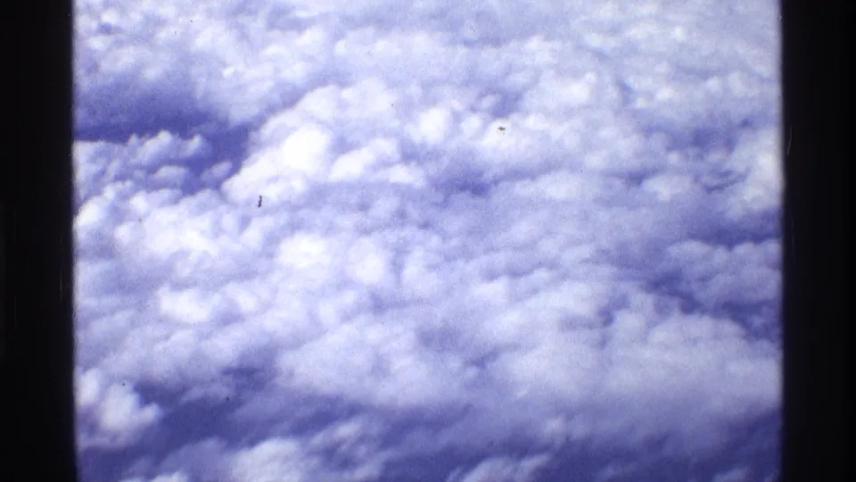 Aerial cloud layer in 1970 8mm footage, with dark vertical window or film edges and no visible ground or landmarks.