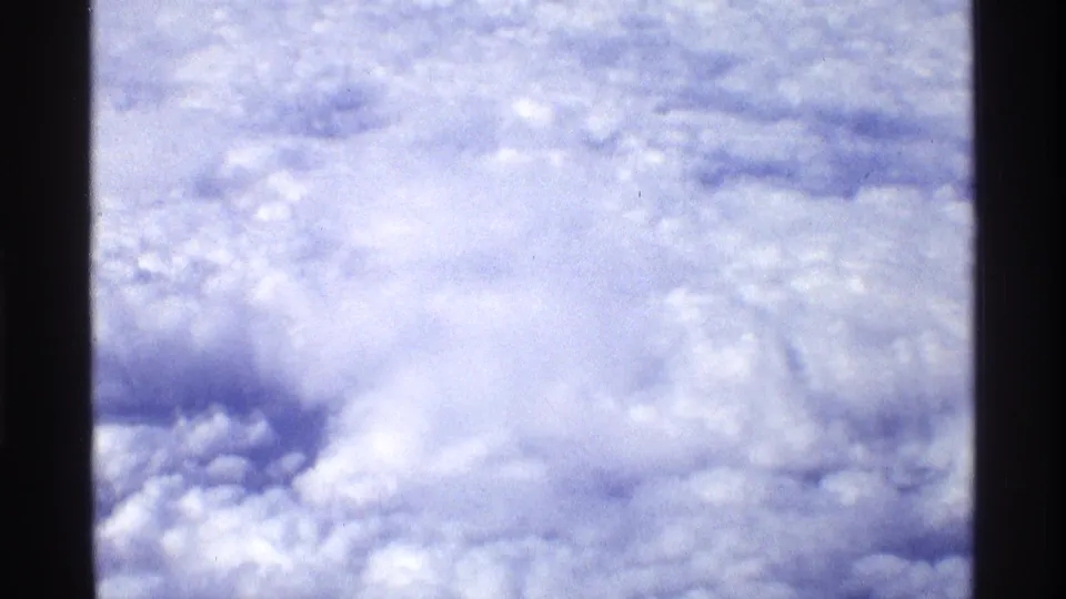 Bright, soft 8mm aerial view over a cloud field, likely filmed from an airplane window during the 1970 home-movie clip.