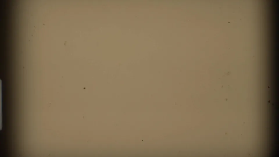 A beige blank 8mm frame with dark edge shading, light vignetting, and small dust marks from the film scan.