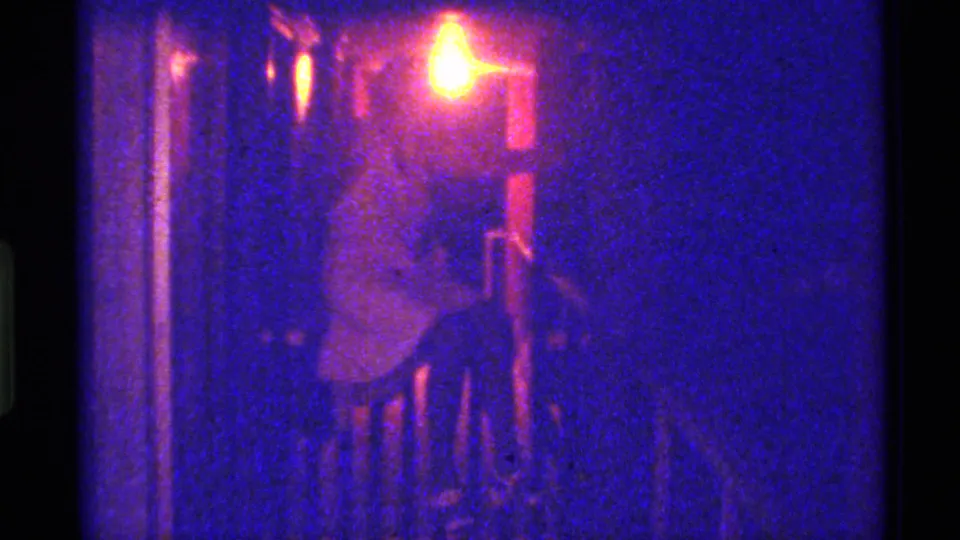 1973 Florida home-movie frame with a seated adult woman in a white or pale dress, partly obscured by shadow and film grain.