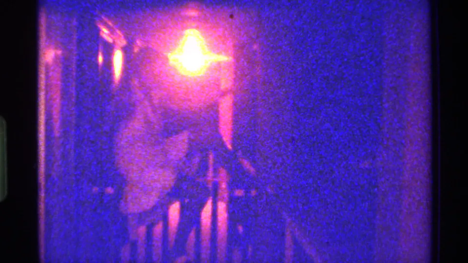 1973 Florida 8mm still of a seated adult woman in a pale dress, her face and body softened by flare, grain, and low light.
