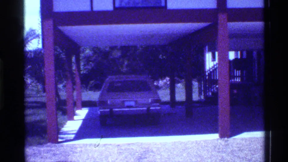 1973 Florida 8mm frame showing a sedan parked beneath a raised house carport with support posts and a driveway.