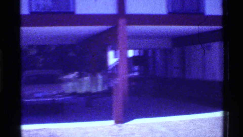 1973 Florida home-movie frame with motion blur across a carport, support post, parked sedan, driveway, and house exterior.