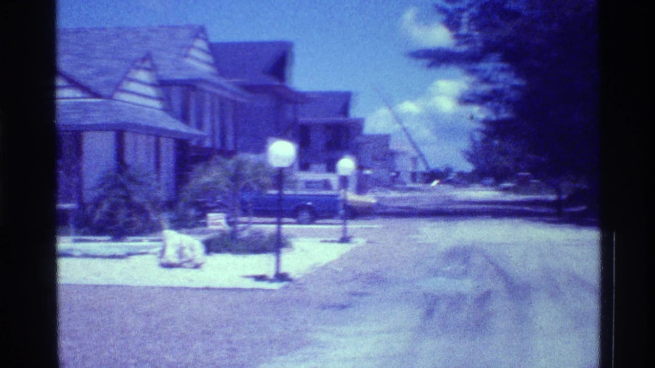 Quiet residential street with gabled houses, globe lamps, and a parked blue car.