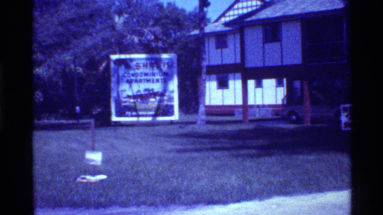 Condominium sign on a lawn near a two-story building.