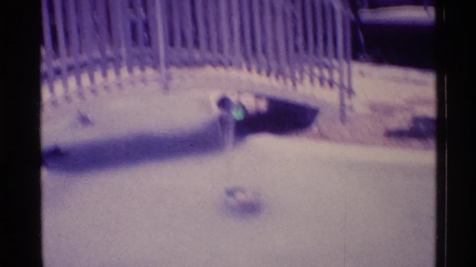 Soft, purple-shifted 1973 Florida 8mm frame of a resort water feature, white bridge, fence, and small vertical spray.