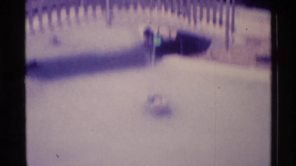 1973 Florida home-movie frame showing pale fountain water, a curved metal bridge or railing, and dark edge shadows.