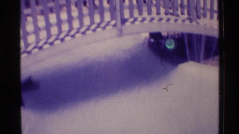 Soft 1973 Florida home-movie frame with fountain water, bridge railing, and a dark structure at the water's edge.