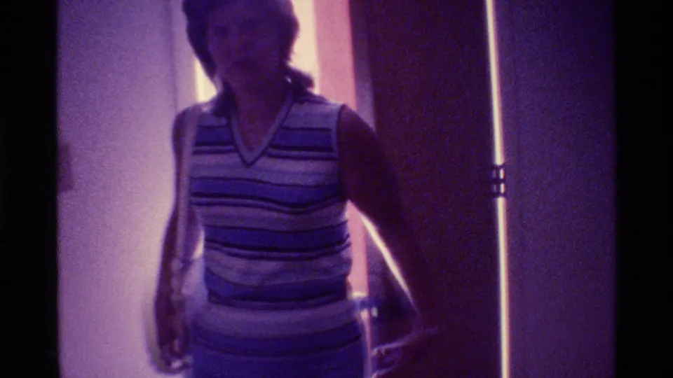 1973 Florida home-movie frame of an adult woman in a striped sleeveless top near a doorway or entrance.