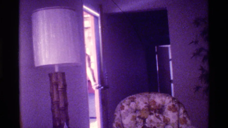 Florida 1973 home interior with bamboo-style floor lamp, floral armchair, doorway, and refrigerator, seen with purple 8mm color cast.