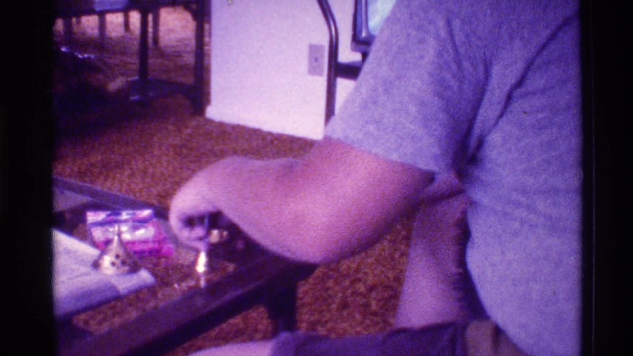 Person in a gray T-shirt reaches toward small objects on a glass-topped table.