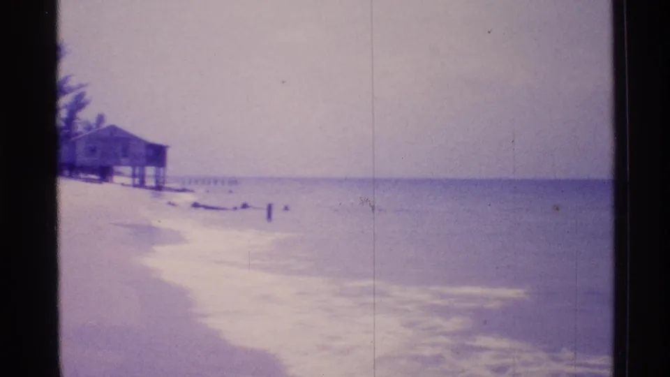 1973 Florida shoreline view with a raised beach house, pale surf, horizon, and open water in soft 8mm color.