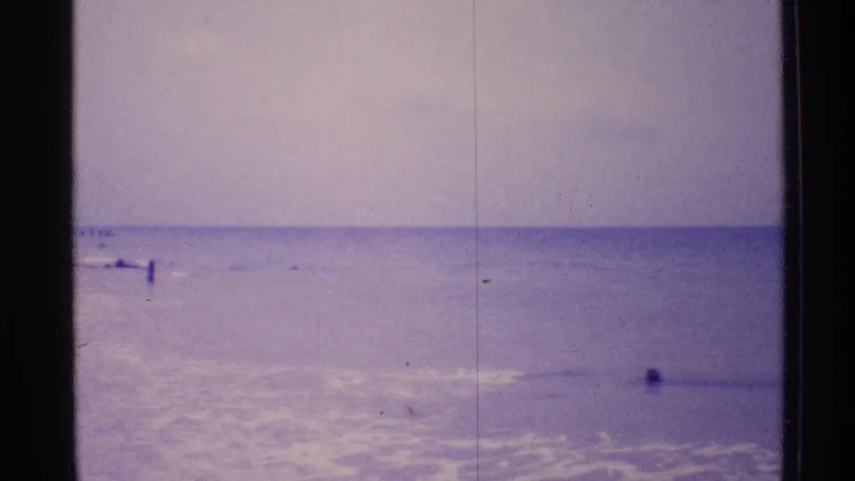1973 Florida beach footage showing low surf, horizon, shoreline posts, and a small distant figure-like shape in the water.