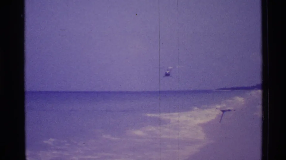 1973 Florida 8mm frame of open ocean, low horizon, breaking surf, and a small indistinct speck above the water.