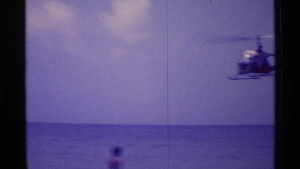 A low helicopter pass is seen near the edge of the 8mm frame above the Florida ocean, with soft focus and purple film aging.