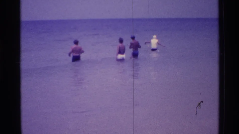 Several beachgoers wade in the Florida shallows at the end of the 1973 8mm clip, with the helicopter no longer prominent.