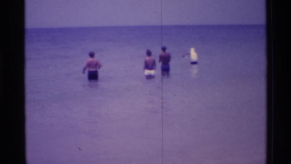 1973 Florida beach home-movie frame showing people in swimwear standing in shallow ocean water near a flat horizon.