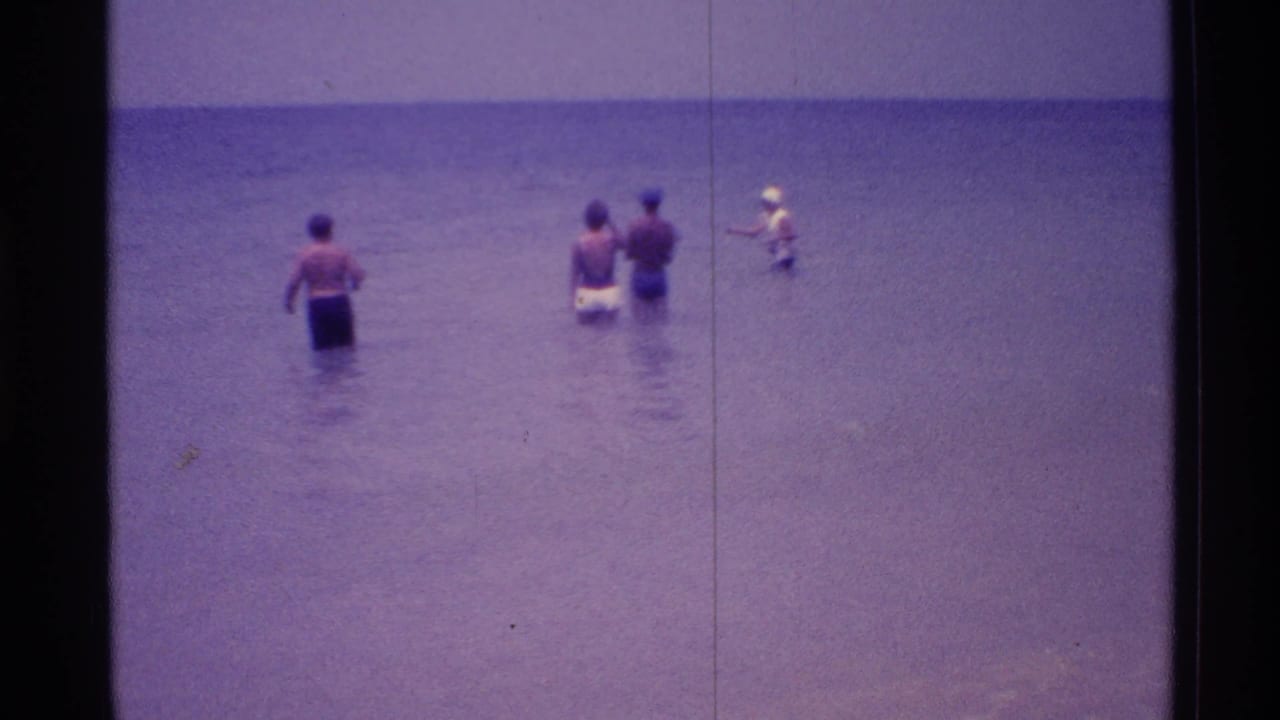 People stand in shallow ocean water as one figure appears to hold a fishing rod.