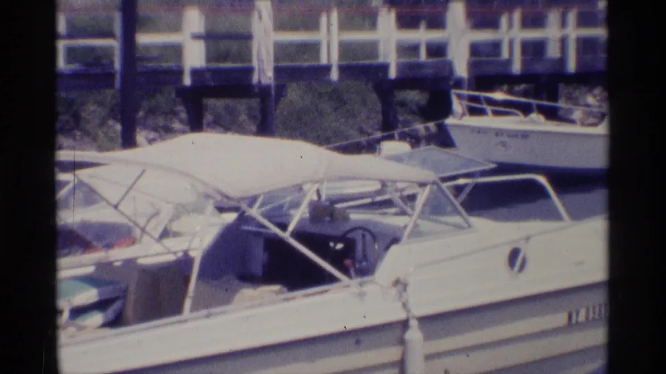 Close 1973 New York 8mm view of a white motorboat with canopy frame, neighboring boats, dock railing, and marina water.