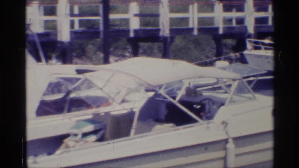 1973 New York 8mm frame of a docked white motorboat, with canopy frame, cockpit area, and nearby boats in the background.