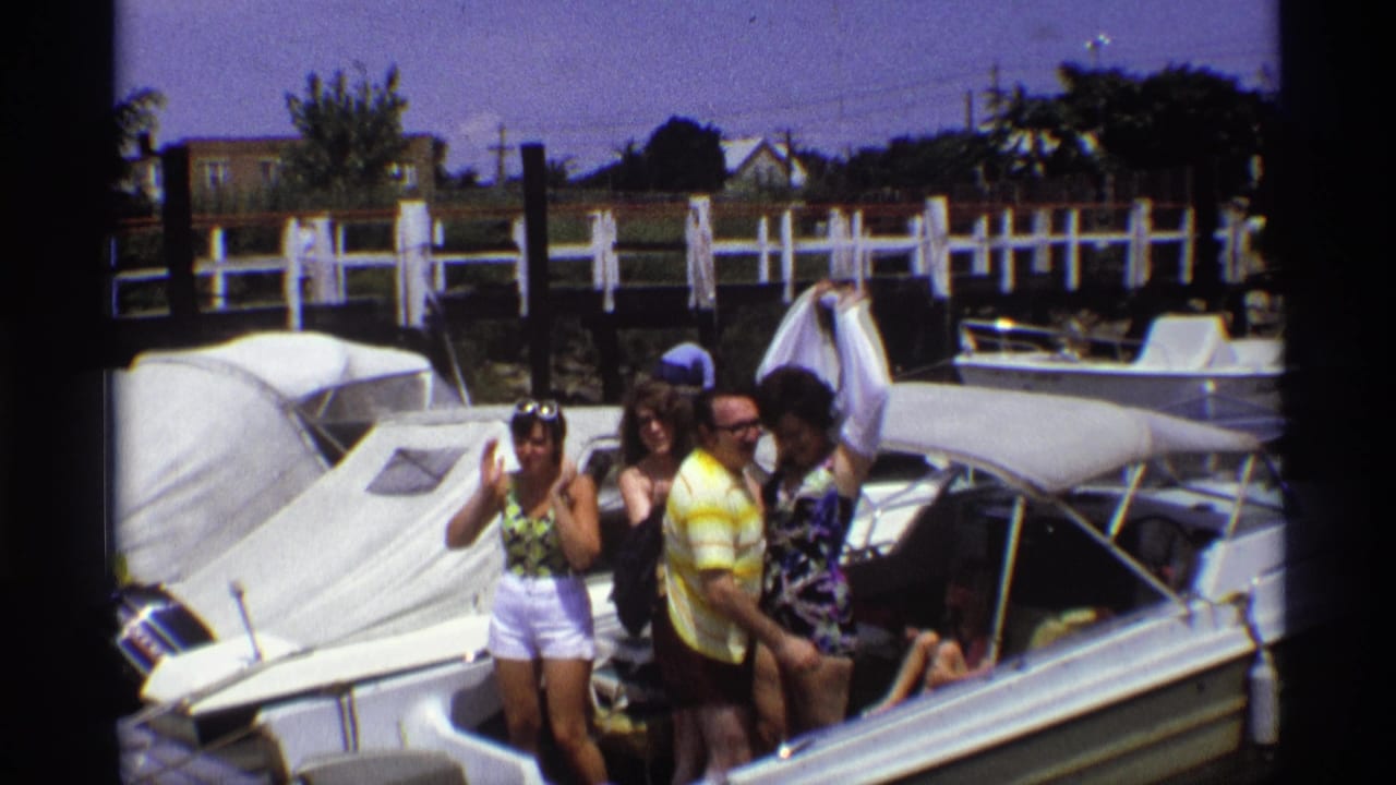Young adults stand on a white motorboat at a sunny marina.