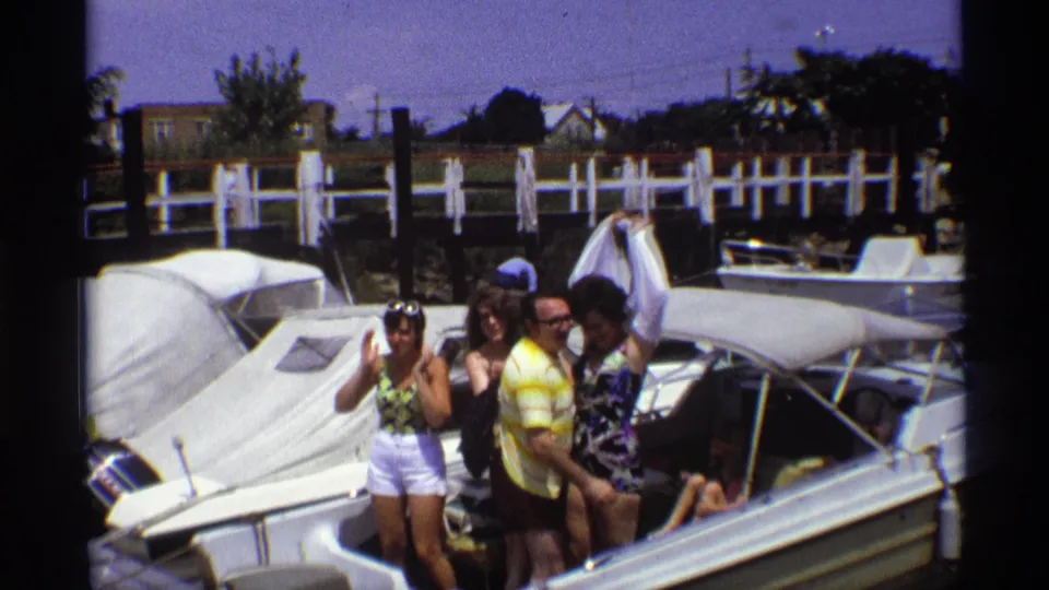 In 1973 New York home-movie footage, young adults gather on a white motorboat beside docks and other boats.