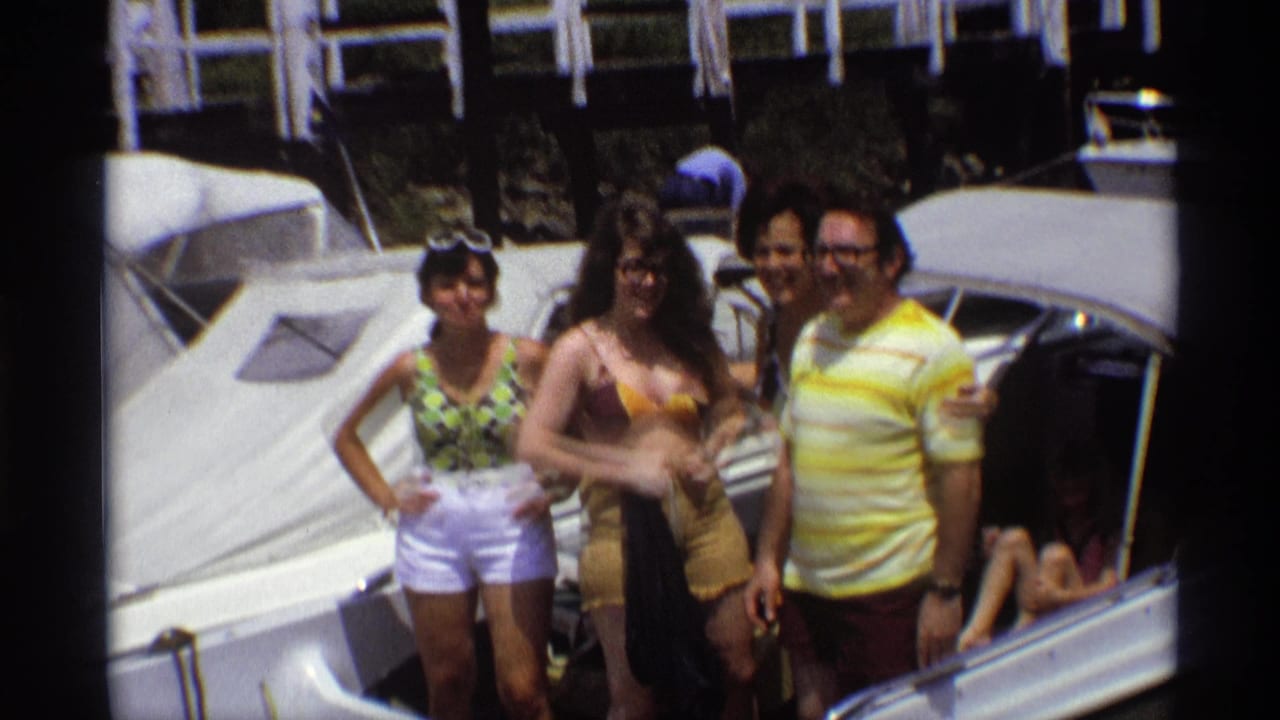 A woman in white shorts, a woman in swimwear, and two men stand on or beside a white boat in the 1973 marina scene.