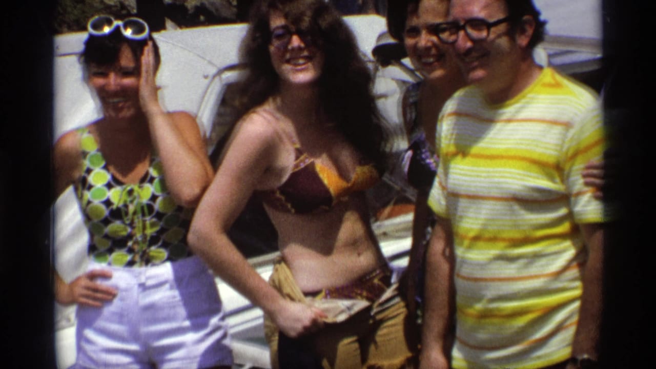 Four adults smiling on a boat in summer clothing and swimwear.