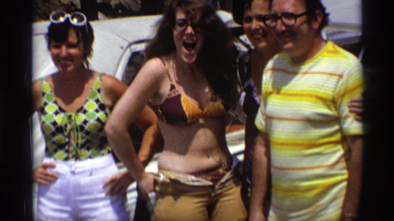 Adults laugh and pose together on a boat in swimwear and summer clothes.