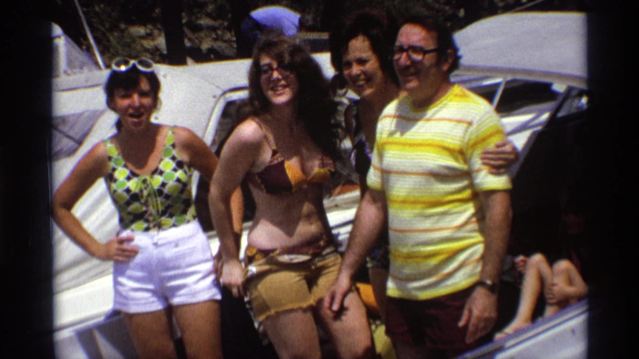 Four adults pose on a boat in 1973 New York home-movie footage, with swimwear, sunglasses, and a partially visible seated person at right.