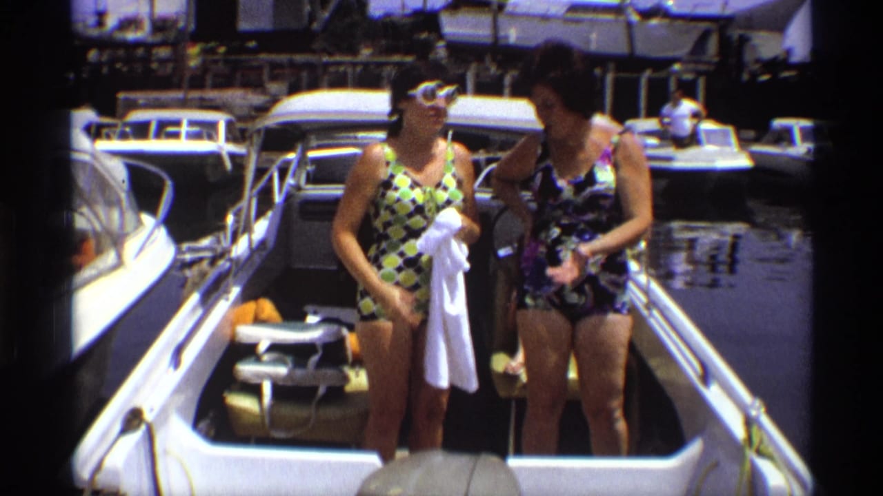In 1973 New York home-movie footage, two women in patterned swimsuits stand on a motorboat beside docked boats.