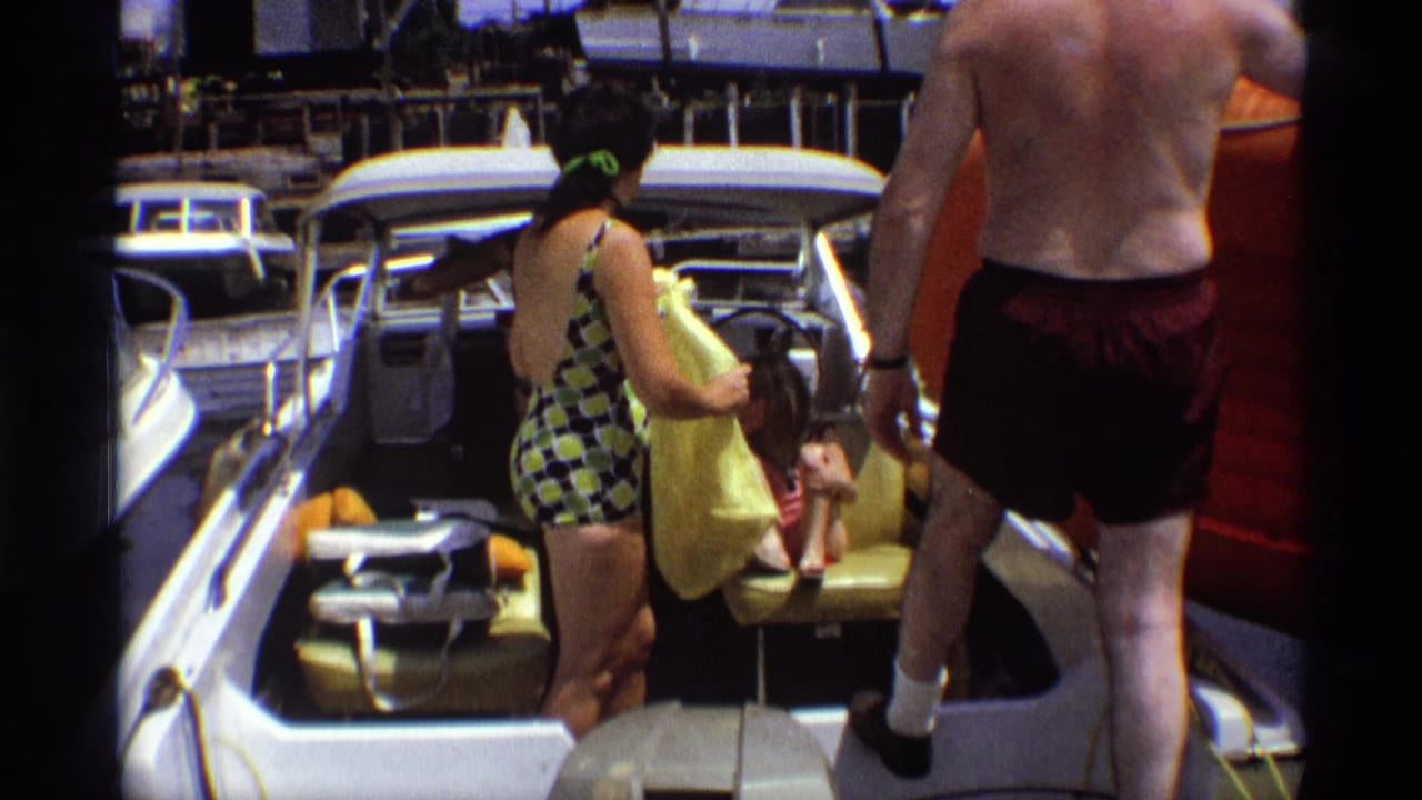 At the end of the 1973 New York marina clip, a woman turns with clothing while a shirtless man boards the motorboat.
