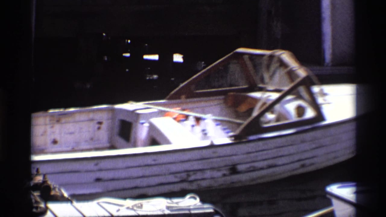 A closer 8mm view shows the weathered side of the white motorboat, its windshield, and dockside equipment in New York, 1973.