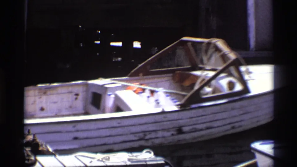 A closer 8mm view shows the weathered side of the white motorboat, its windshield, and dockside equipment in New York, 1973.